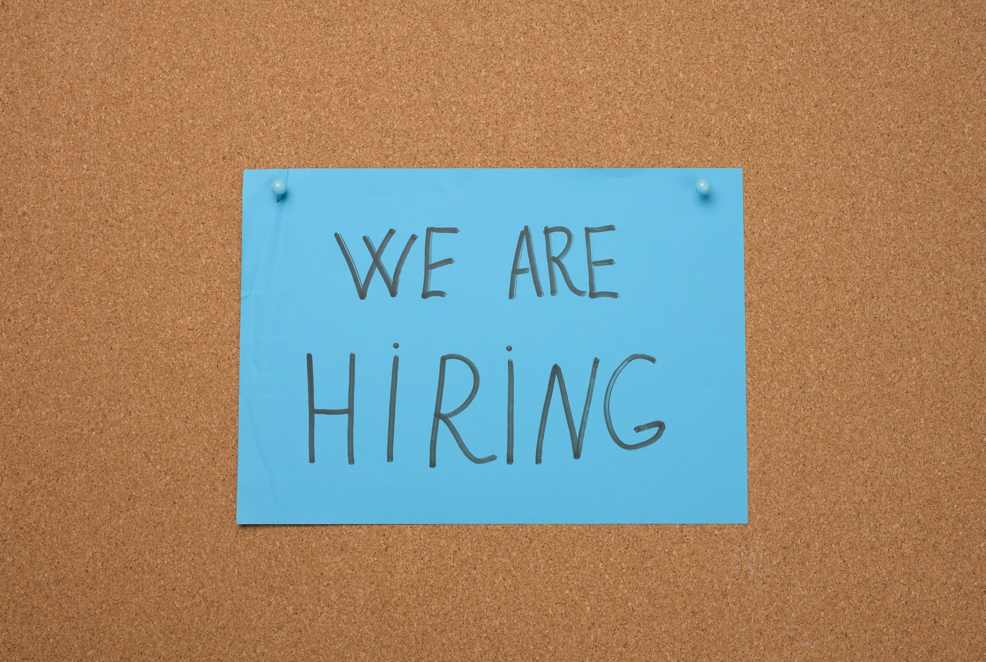 Blue sheet of paper with an inscription on a brown cork board. Recruitment concept, vacancy